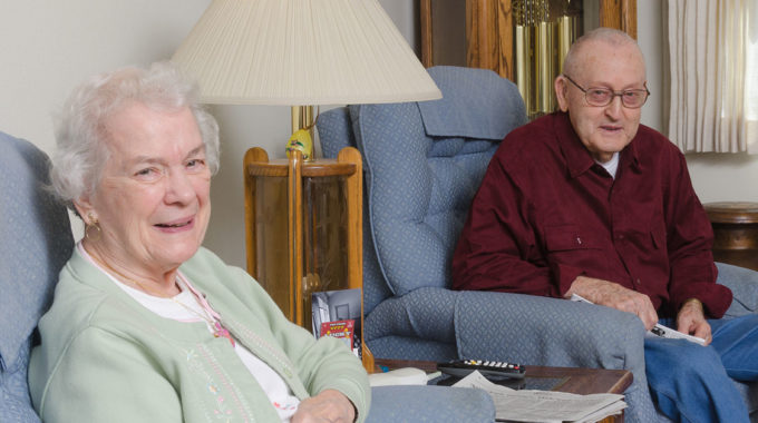 An Elderly Wife Sits At Home With Her Husband Who Is On Hospice