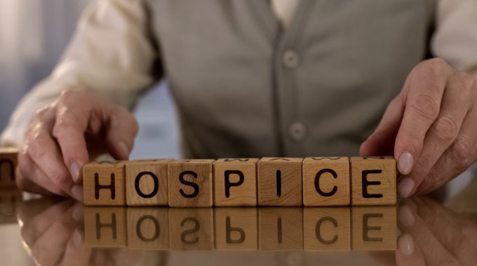 Senior Man Spelling Out Hospice With Wooden Blocks.