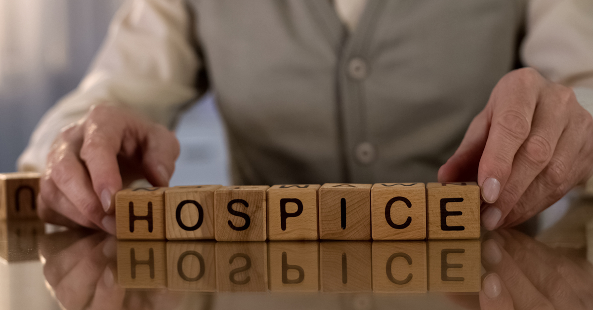 Senior Man Spelling Out Hospice With Wooden Blocks.