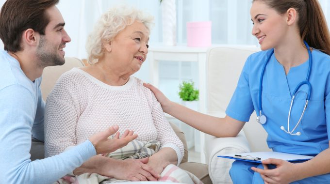 Mother And Her Adult Son Speaking To A Nurse In Their Home.