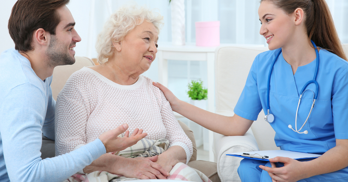 Mother And Her Adult Son Speaking To A Nurse In Their Home.