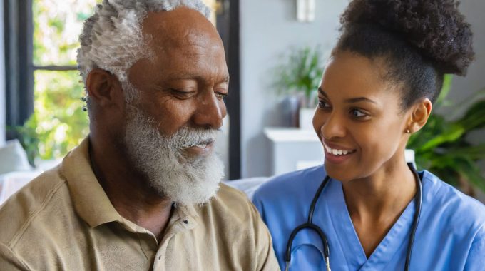 African American Nurse Lifting The Spirits Of An Elderly Man In Hospice.